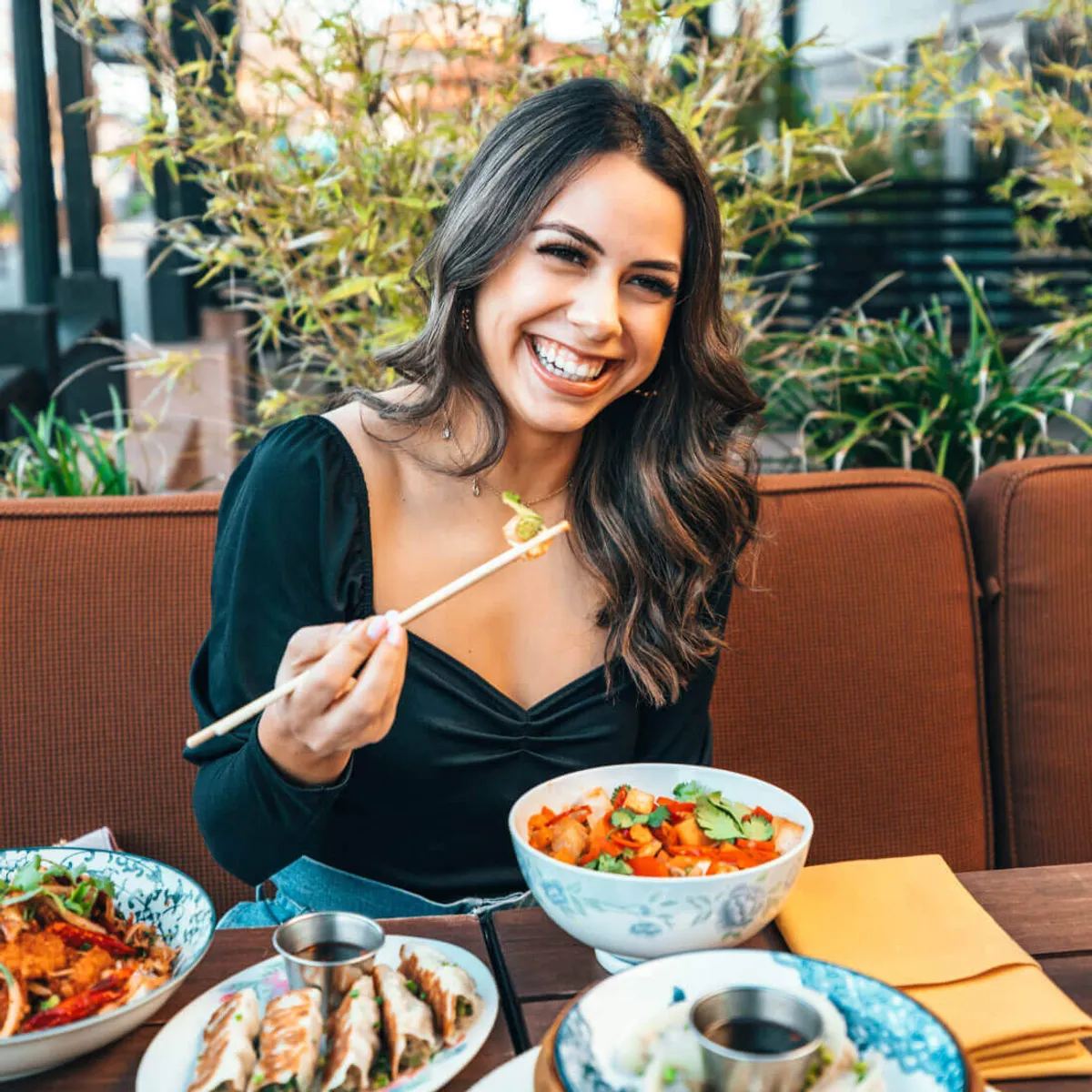 Woman laughing while eating with chopsticks at a restaurant table